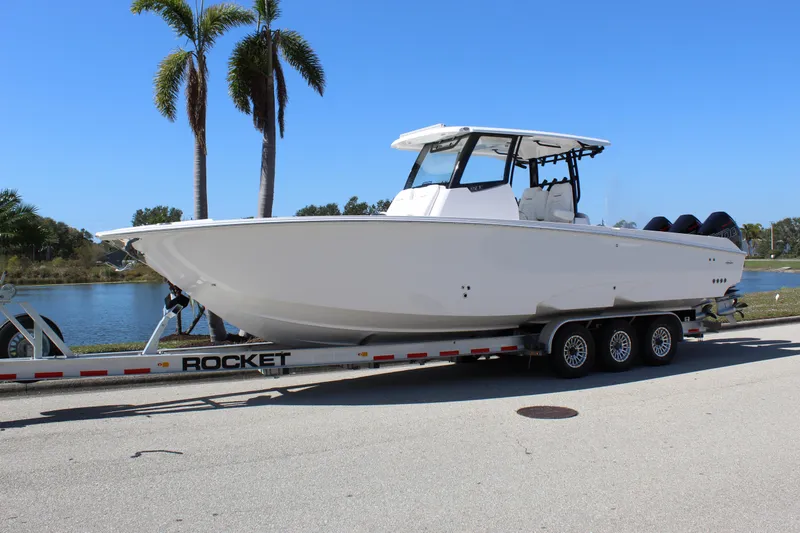  Yacht Photos Pics 2024 Fountain 32 NX boat on trailer, parked near palm trees and water.