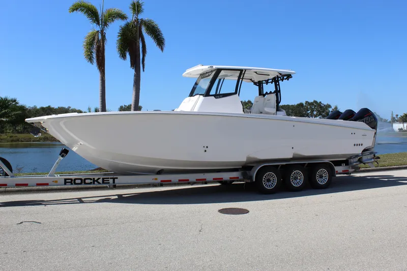  Yacht Photos Pics 2024 Fountain 32 NX boat on trailer, parked near palm trees and water.