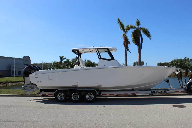  Yacht Photos Pics 2024 Fountain 32 NX boat on trailer, parked near palm trees under clear blue sky.