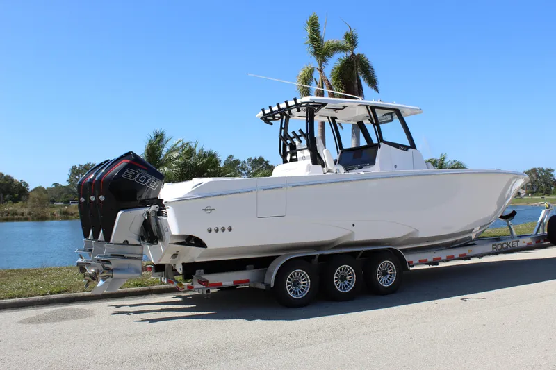  Yacht Photos Pics 2024 Fountain 32 NX boat on trailer by a lake, featuring triple outboard engines.