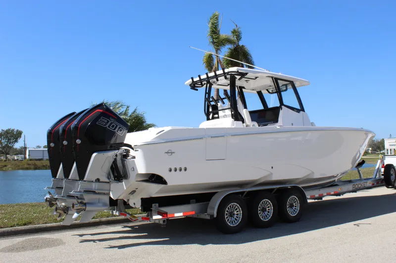  Yacht Photos Pics 2024 Fountain 32 NX boat on trailer, triple engines, parked near water under clear blue sky.
