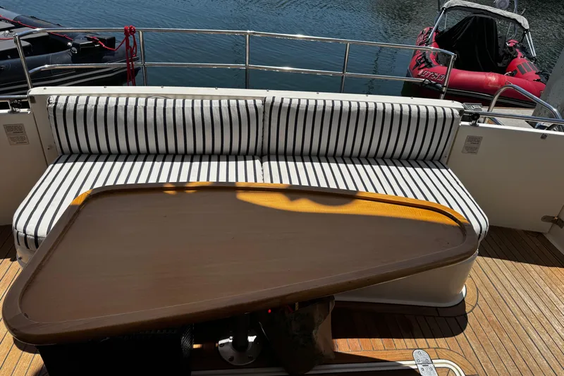 My Way Yacht Photos Pics Striped seating and wooden table on 2001 Fairline 55 yacht deck by the water.