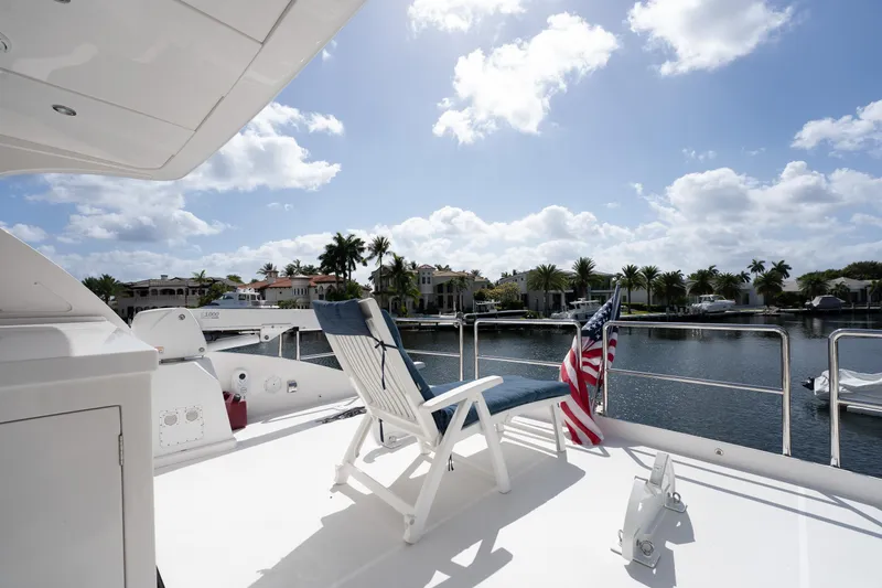 Passion Yacht Photos Pics Luxurious Horizon PC52 yacht deck with chair, American flag, and waterfront view under blue sky.