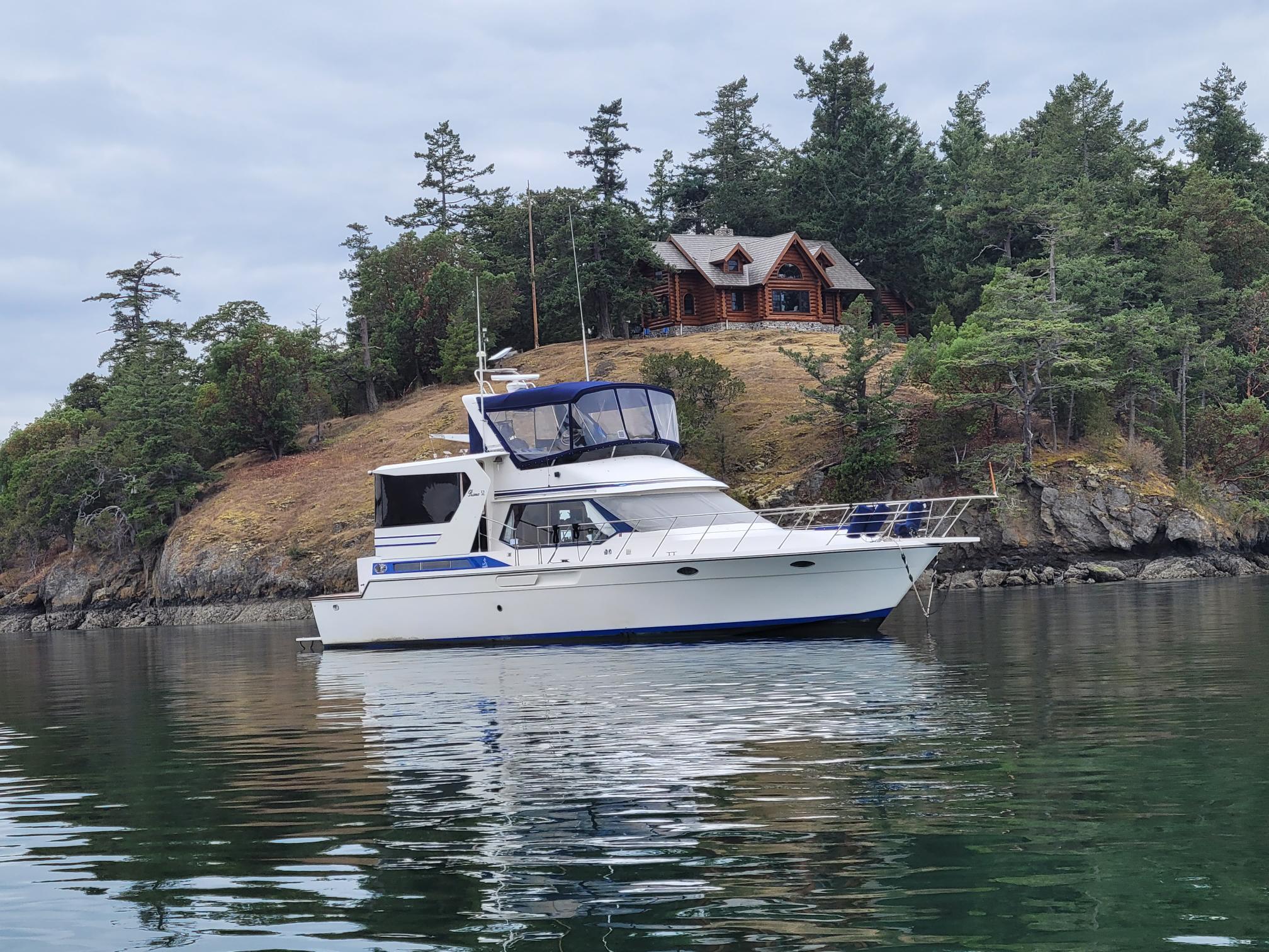 1989 Prima 52 Cockpit Motor Yacht on calm water near a forested shoreline.