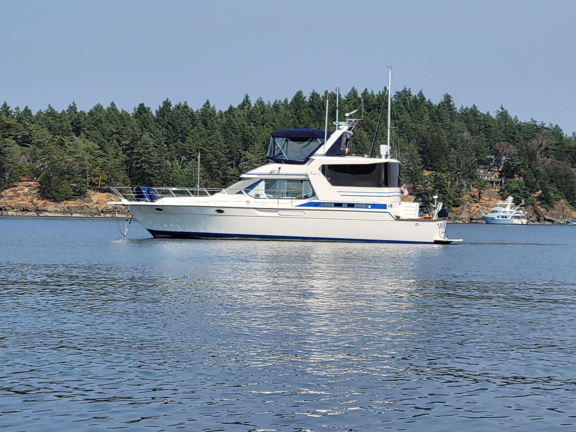 1989 Prima 52 Cockpit Motor Yacht on calm water, forested shoreline in background.