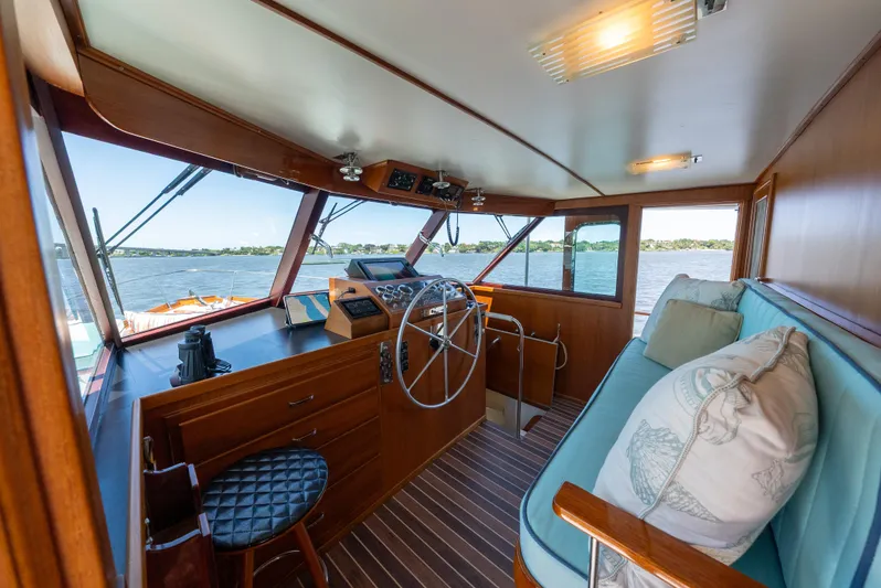 Absolute Yacht Photos Pics 1970 Trumpy houseboat interior with wooden helm, blue seating, and scenic water view.