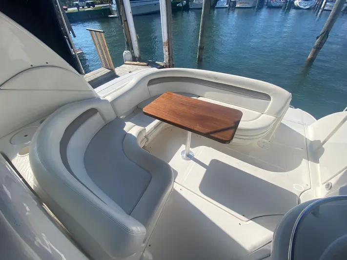 No Fly Zone Yacht Photos Pics 2003 Sea Ray 340 Sundancer boat interior with curved seating and wooden table by the dock.