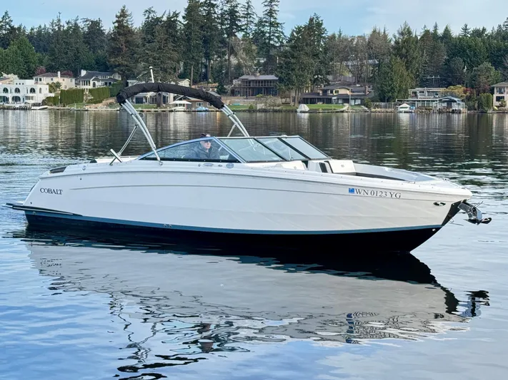  Yacht Photos Pics 2023 Cobalt R8 boat on a serene lake with waterfront homes and trees in the background.