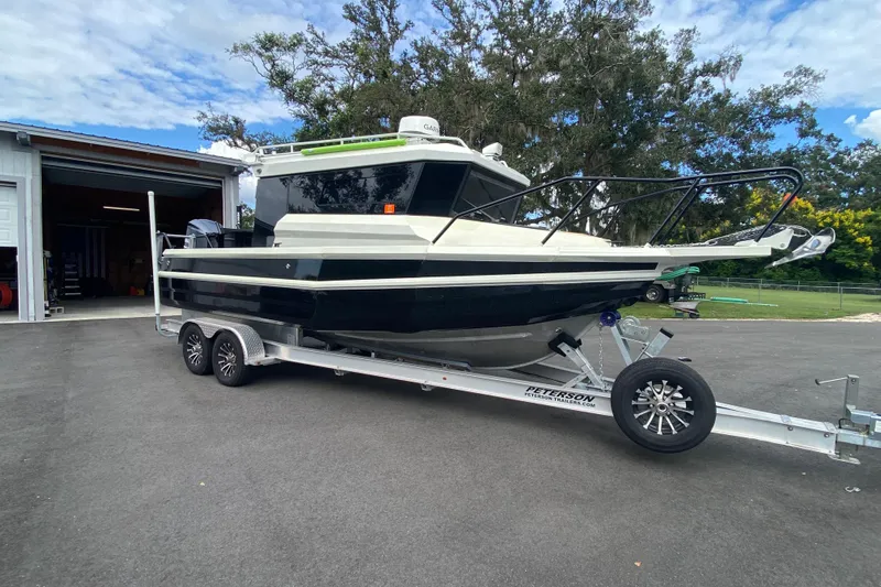  Yacht Photos Pics 2024 Sea King 260 boat on trailer, parked outside a garage, surrounded by trees.