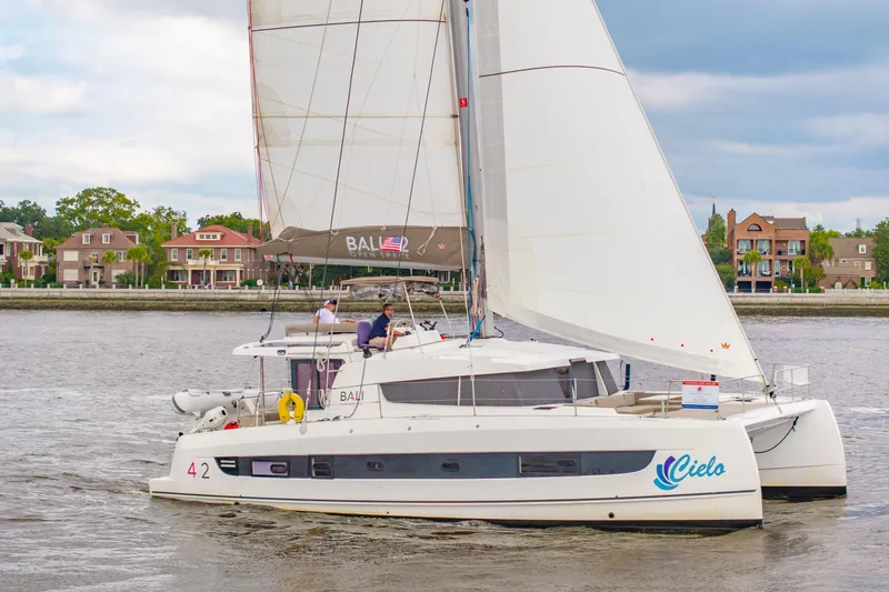 Cielo Yacht Photos Pics 2023 Bali 4.2 catamaran sailing near waterfront homes under cloudy skies.