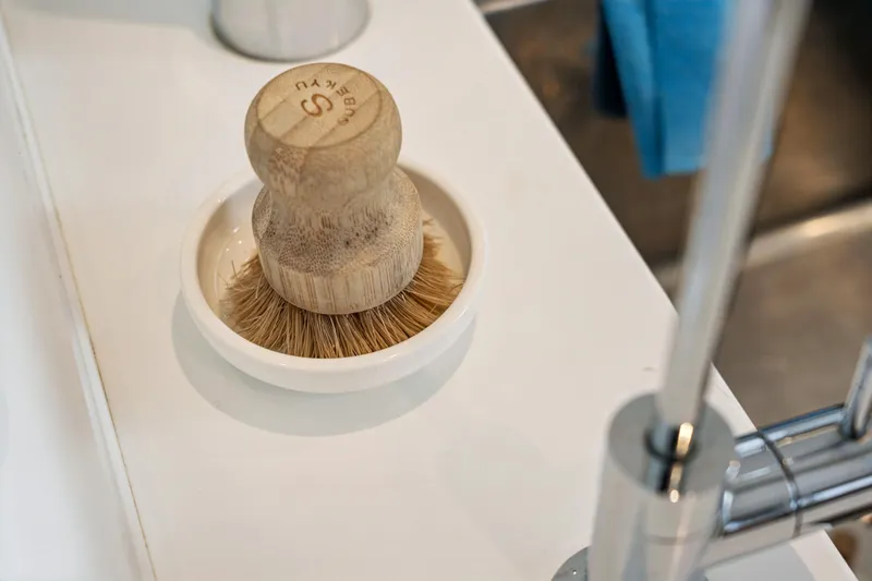 Cielo Yacht Photos Pics Wooden dish brush on a white kitchen countertop near a modern faucet.