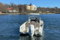 Nimbus T8 boat cruising on a calm lake with scenic shoreline and buildings in the background.