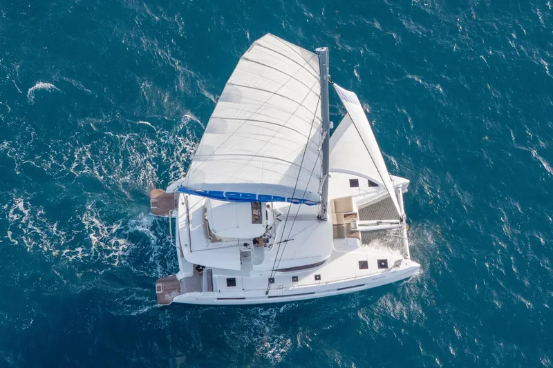 Bellissima Yacht Photos Pics Aerial view of 2024 Lagoon 51 catamaran sailing on blue ocean waters.