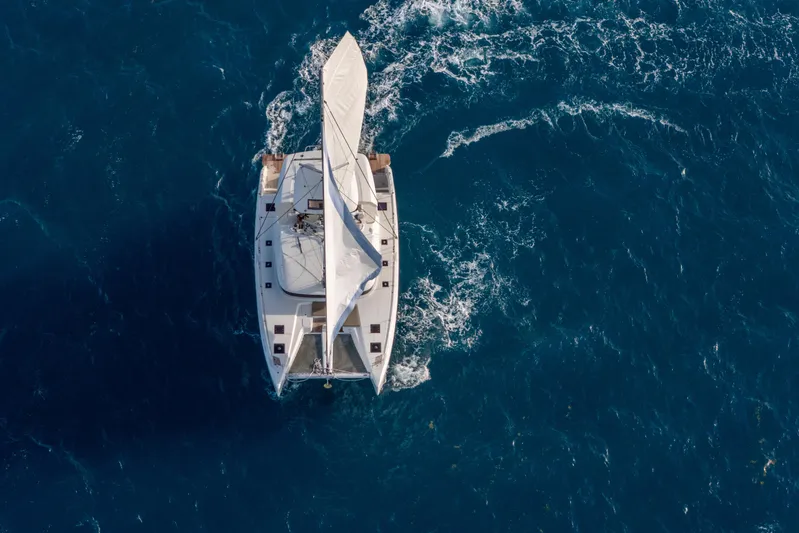 Bellissima Yacht Photos Pics Aerial view of 2024 Lagoon 51 sailing catamaran navigating through blue ocean waters.