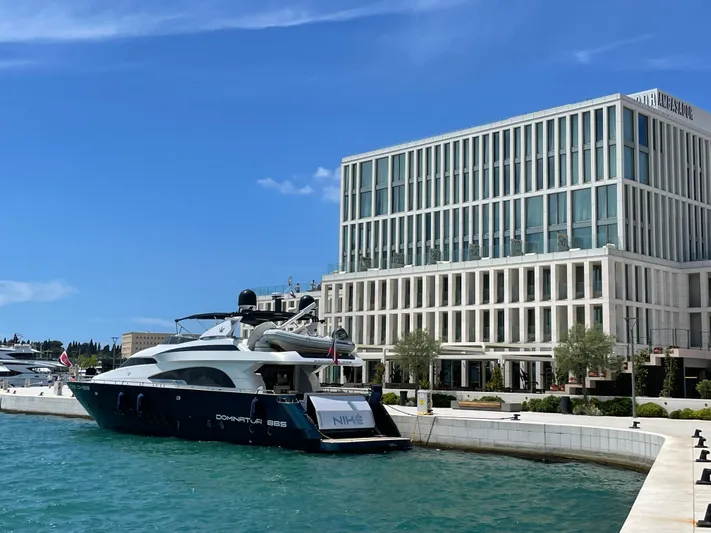 Nike Yacht Photos Pics Luxury yacht Dominator 860 docked near modern waterfront building, clear blue sky.