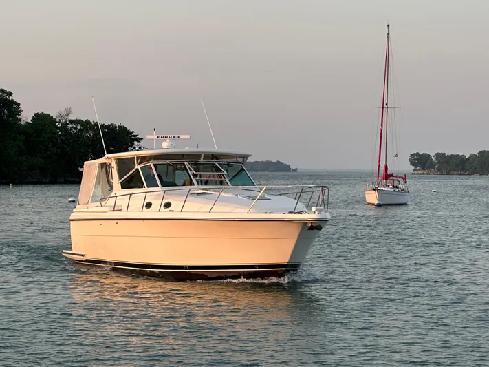 Nice Aft Yacht Photos Pics 1998 Tiara Yachts 4000 Express cruising on a serene lake with a sailboat nearby.