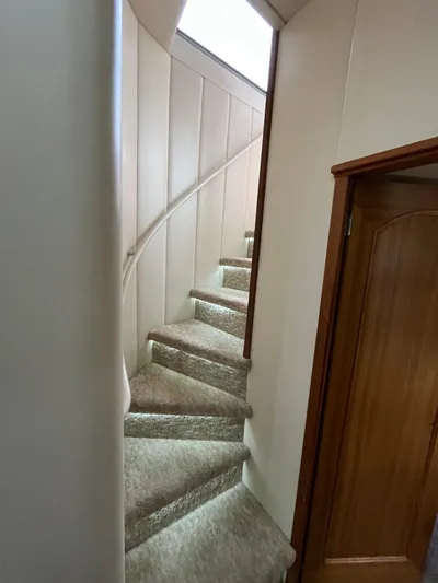Our Time Yacht Photos Pics Curved staircase inside 2001 Bayliner 5788 Pilot House Motoryacht, featuring carpeted steps and wooden door.