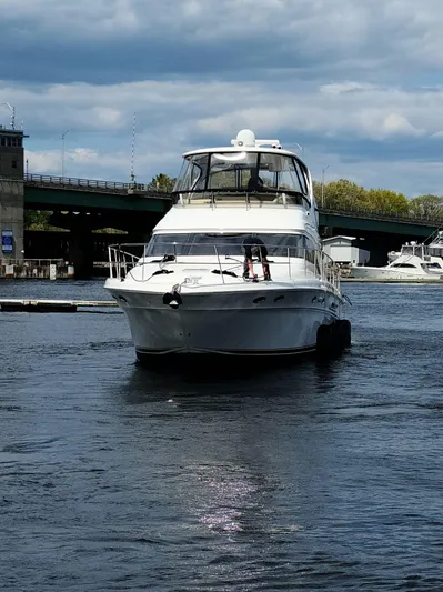  Yacht Photos Pics 2002 Sea Ray 56 Sedan Bridge yacht on a calm river under a cloudy sky.