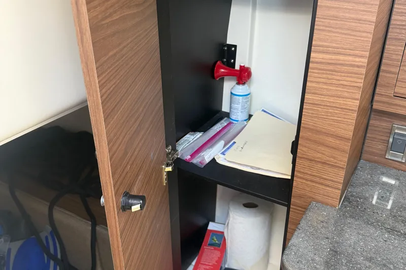  Yacht Photos Pics Open cabinet on 2021 Boston Whaler 325 Conquest, showing storage items and wooden finish.