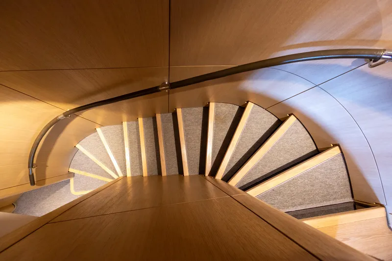 Grand Cru Yacht Photos Pics Curved wooden staircase inside 1995 Baglietto 49M yacht, featuring elegant design and modern lighting.