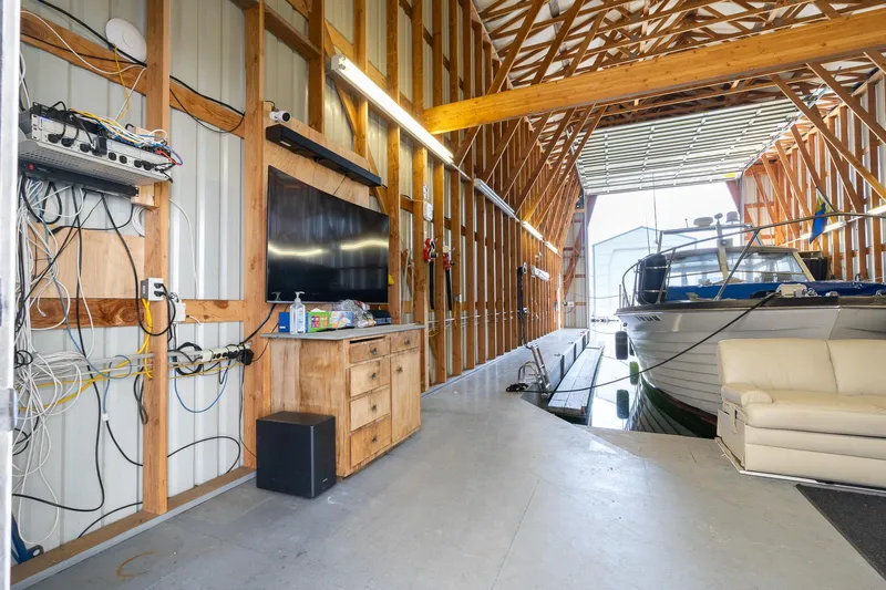  Yacht Photos Pics Modern boathouse interior with boat, TV, and sofa, featuring exposed wooden beams.