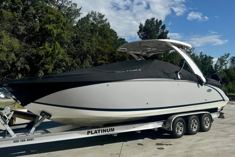 Drama Free Yacht Photos Pics 2022 Cobalt R30 boat on trailer, covered, parked outdoors with trees in background.
