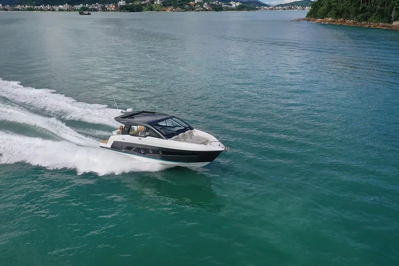  Yacht Photos Pics 2025 Schaefer 380 yacht cruising on clear blue water near a lush coastline.