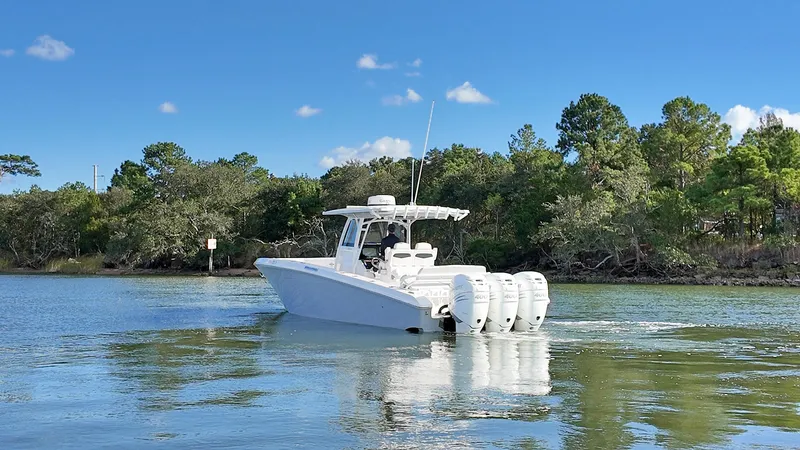  Yacht Photos Pics 2022 Fountain 38TE boat with triple engines on a calm lake, surrounded by trees.