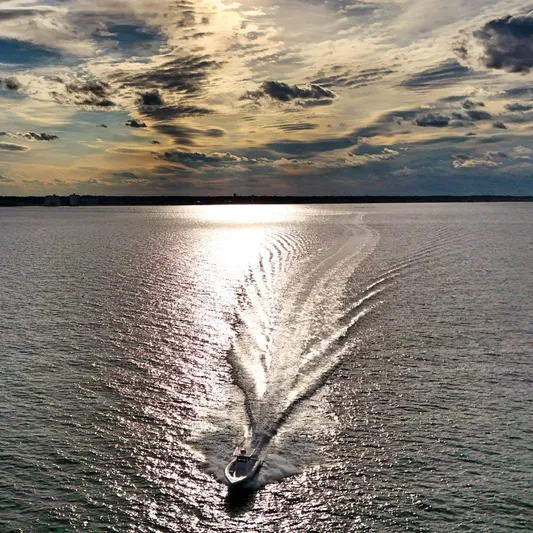  Yacht Photos Pics A 2022 Fountain 38TE boat cruising on a sunlit, tranquil sea under a dramatic sky.