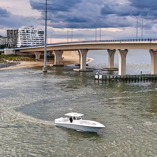  Yacht Photos Pics A 2022 Fountain 38TE boat cruising under a bridge near a sandy shoreline.