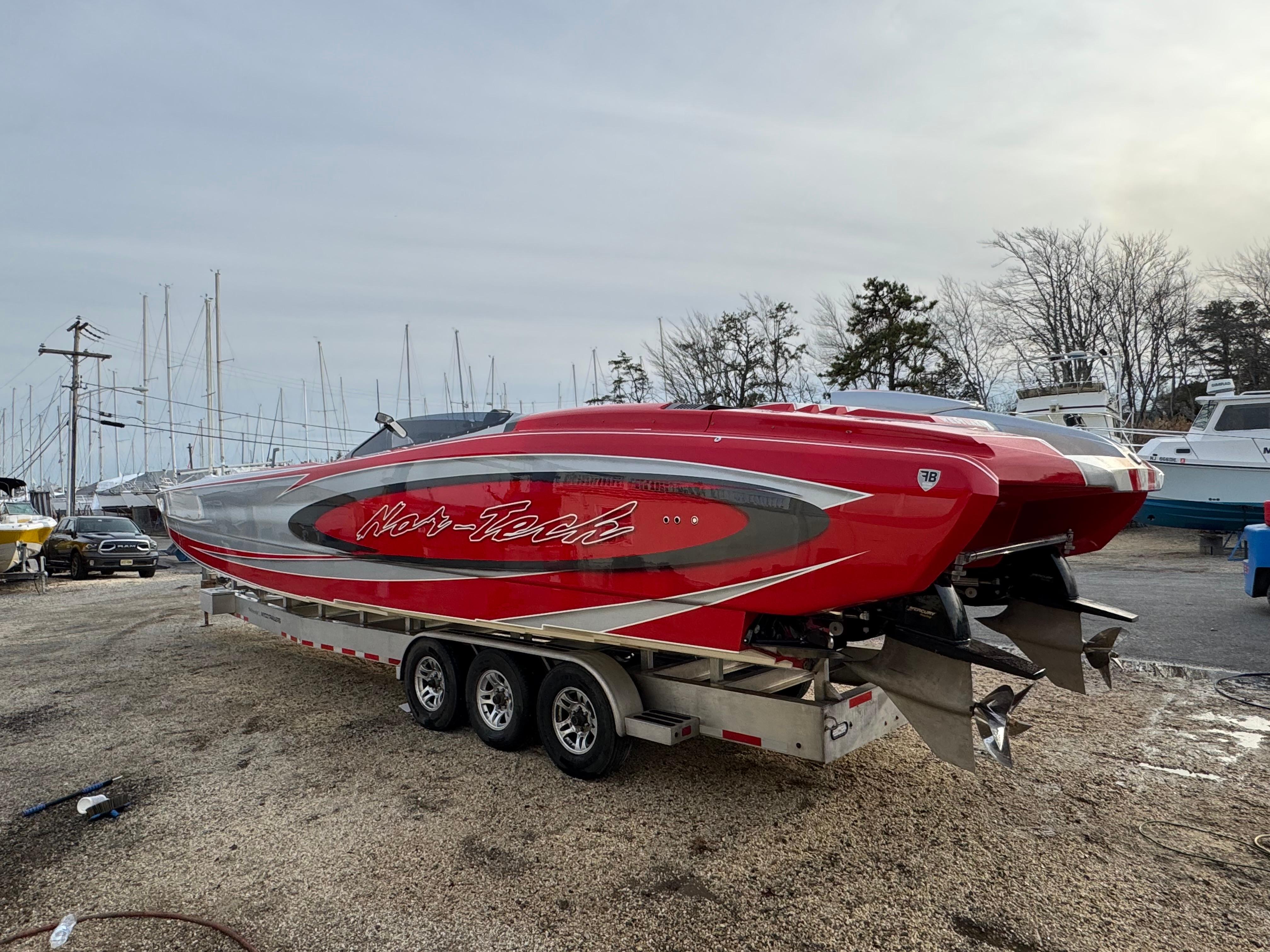 Red 2010 Nor-Tech 4000 Roadster boat on trailer in marina setting.