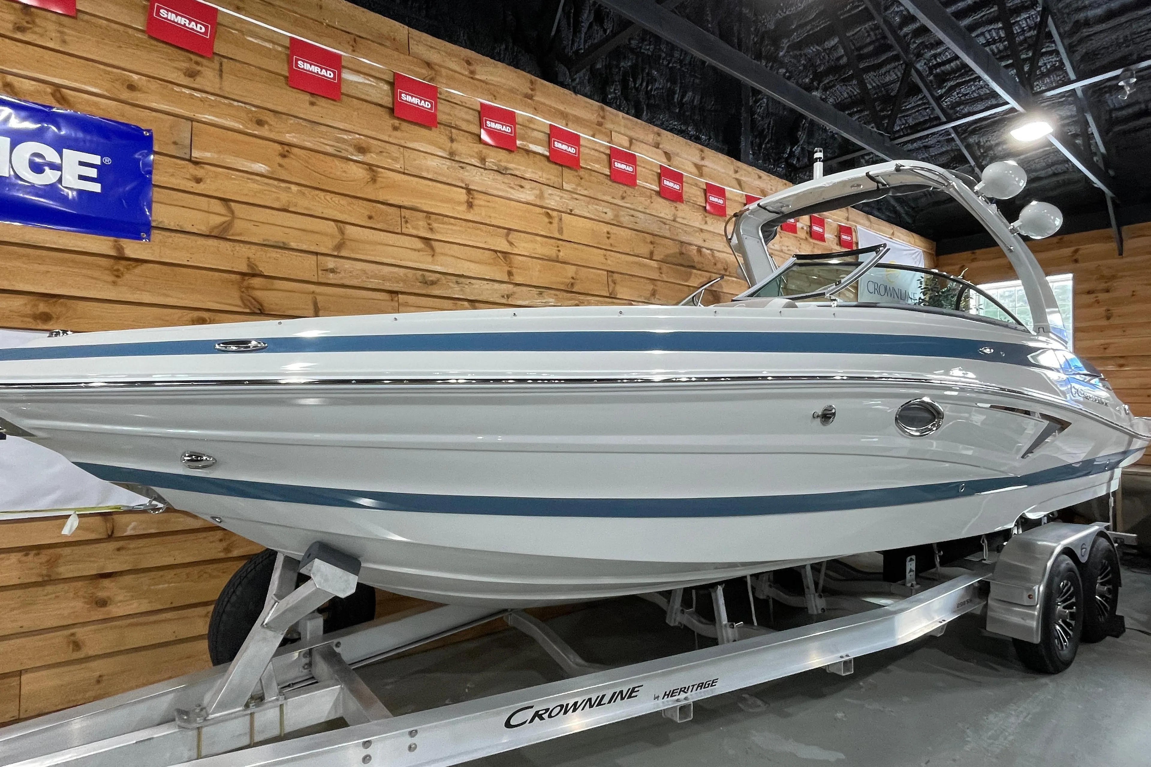 2026 Crownline 298 SS boat on trailer in showroom, wooden wall background.