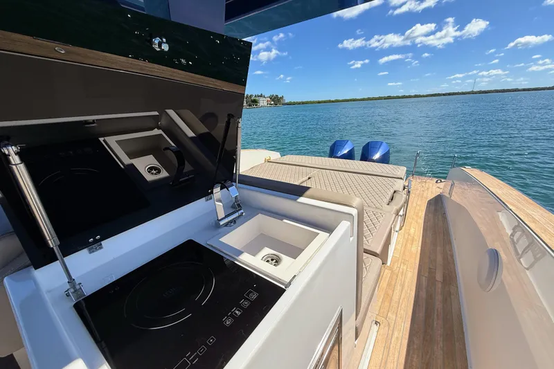 Mine Yacht Photos Pics 2022 Tesoro T38 Outboard boat with outdoor kitchen and seating, overlooking serene water.