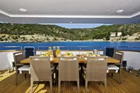 Luxury dining area on Tecnomar 100 yacht, 2009, overlooking serene blue waters and lush hills.
