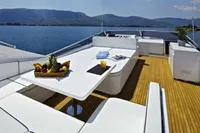 Luxurious Tecnomar 100 yacht deck with dining area, fruit platter, and scenic ocean view.
