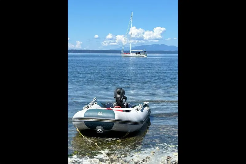 Imagine Yacht Photos Pics Inflatable boat on shore with J Boats J/44 sailboat in the distance, clear blue sky.