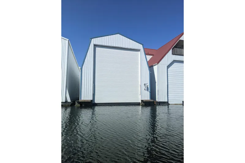  Yacht Photos Pics White custom boathouse on water, built in 1995, with blue sky background.