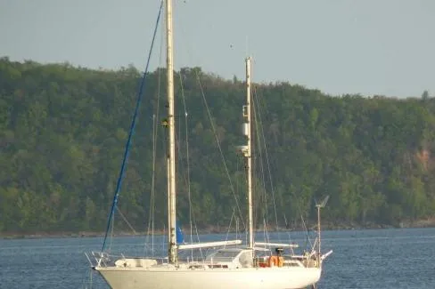 Blue Song Yacht Photos Pics 1984 Amel Maramu 45 sailboat anchored near a lush, forested shoreline.