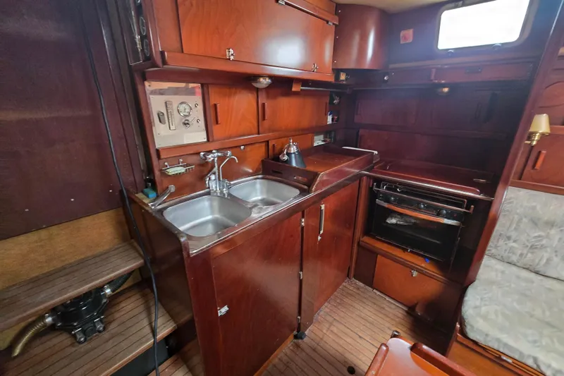 Blue Song Yacht Photos Pics 1984 Amel Maramu 45 yacht interior kitchen with wooden cabinetry and dual sink.