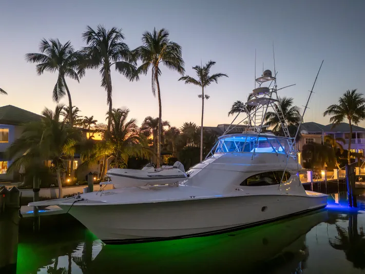 Cast Away Yacht Photos Pics 2008 Hatteras 68 Convertible yacht illuminated at sunset, docked near palm trees.