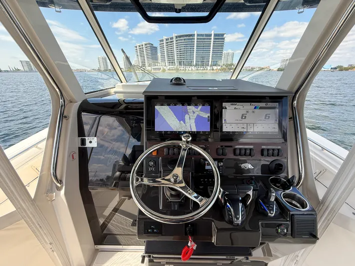 Yacht Photos Pics 2022 Pursuit S 358 Sport boat helm with navigation screens and steering wheel, overlooking waterfront buildings.