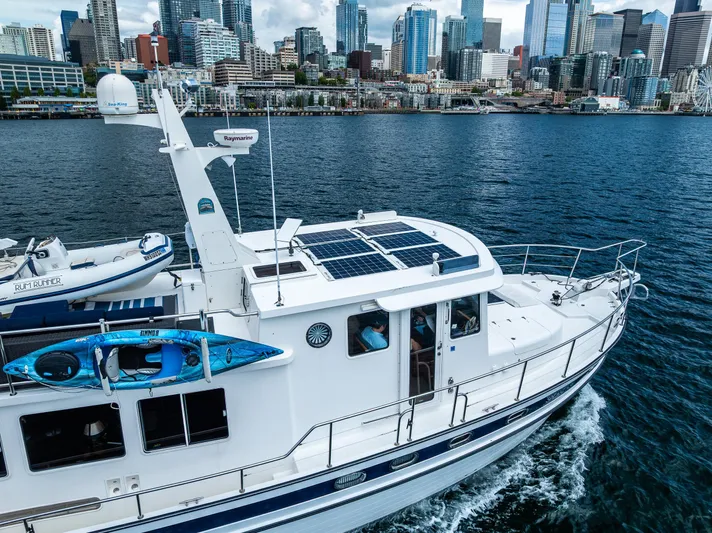 Speakeasy Yacht Photos Pics Nordic Tug 54 (2007) cruising near city skyline, featuring solar panels and kayak on deck.