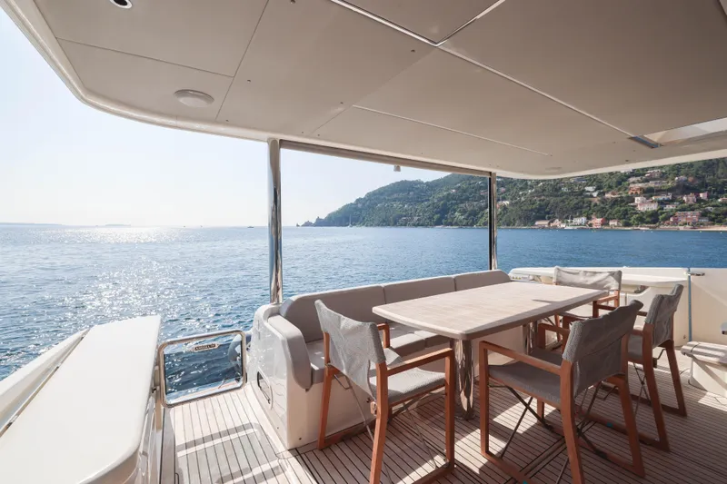  Yacht Photos Pics Luxury yacht Absolute Navetta 68 deck with dining area, overlooking serene ocean and coastal view.