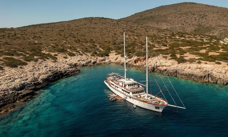 Corsario Yacht Photos Pics Custom RADEŽ d.d. Schooner 2019 anchored in a serene, rocky cove with clear blue water.