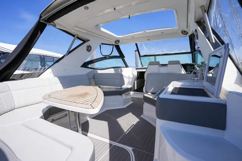  Yacht Photos Pics 2023 Sea Ray Sundancer 320 interior with modern seating, table, and kitchenette under a clear sky.