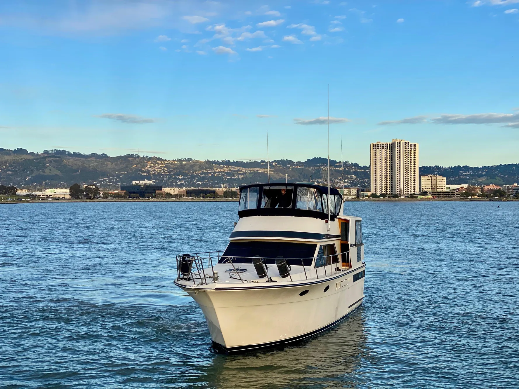 1988 Californian Sundeck Motoryacht cruising on a scenic waterway with city skyline backdrop.