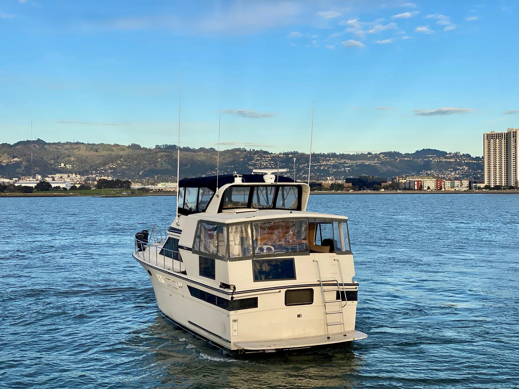 1988 Californian Sundeck Motoryacht cruising on a scenic waterway with cityscape backdrop.