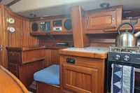 Cozy yacht interior with wooden cabinetry, stove, and kettle, featuring a blue cushioned seat.