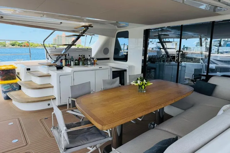 El Nino Yacht Photos Pics Luxurious 2024 Lagoon 65 yacht deck with dining area and bar, overlooking serene waters.