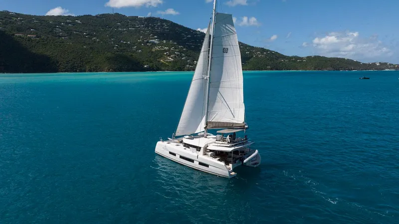  Yacht Photos Pics 2021 Dufour Catamarans 48 sailing in turquoise waters near lush green hills.